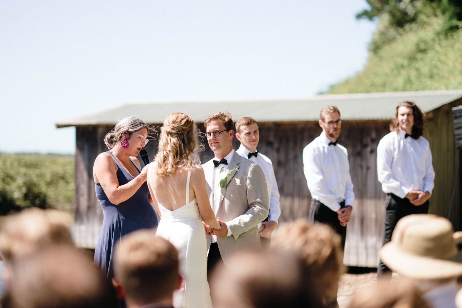 Wedding celebration underway with guests gathered in front of rustic barn structure.