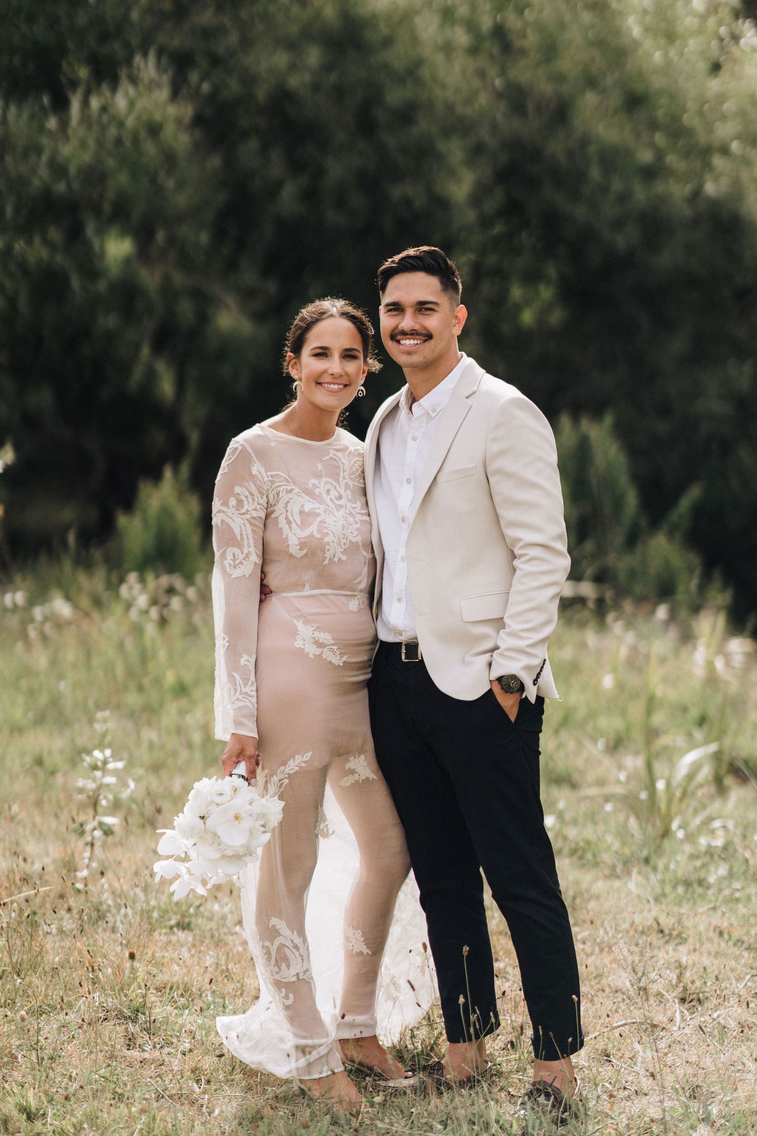 Maternity photoshoot in a sunlit field with white lace dresses and formal attire.