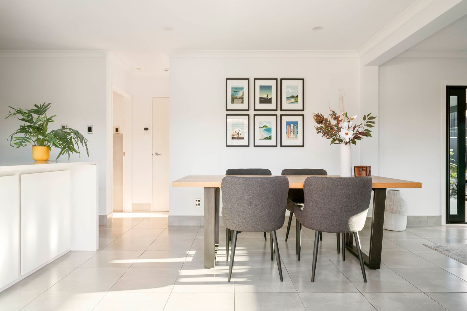 Minimalist white open plan living area featuring hardwood floors and gallery wall art with indoor plants.
