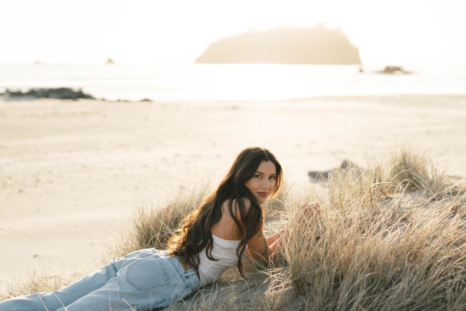 Person relaxes in casual attire among coastal dunes at sunset.
