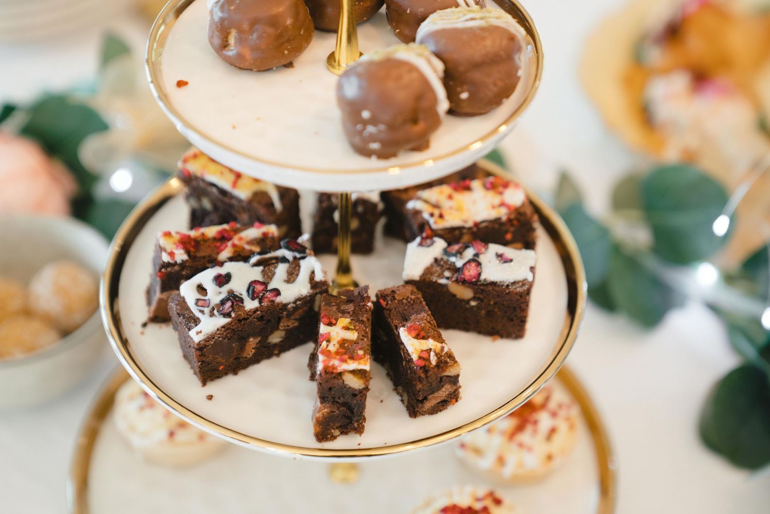 Two-tiered dessert stand displaying chocolate truffles and fudge brownies at an elegant event.