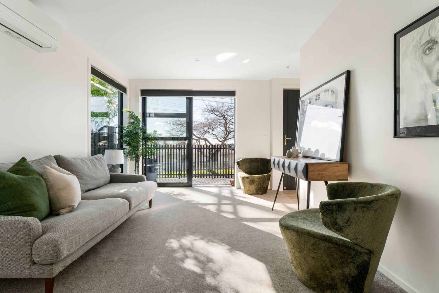 Modern living room with gray sofa, green velvet chairs and glass doors leading to balcony with water views.