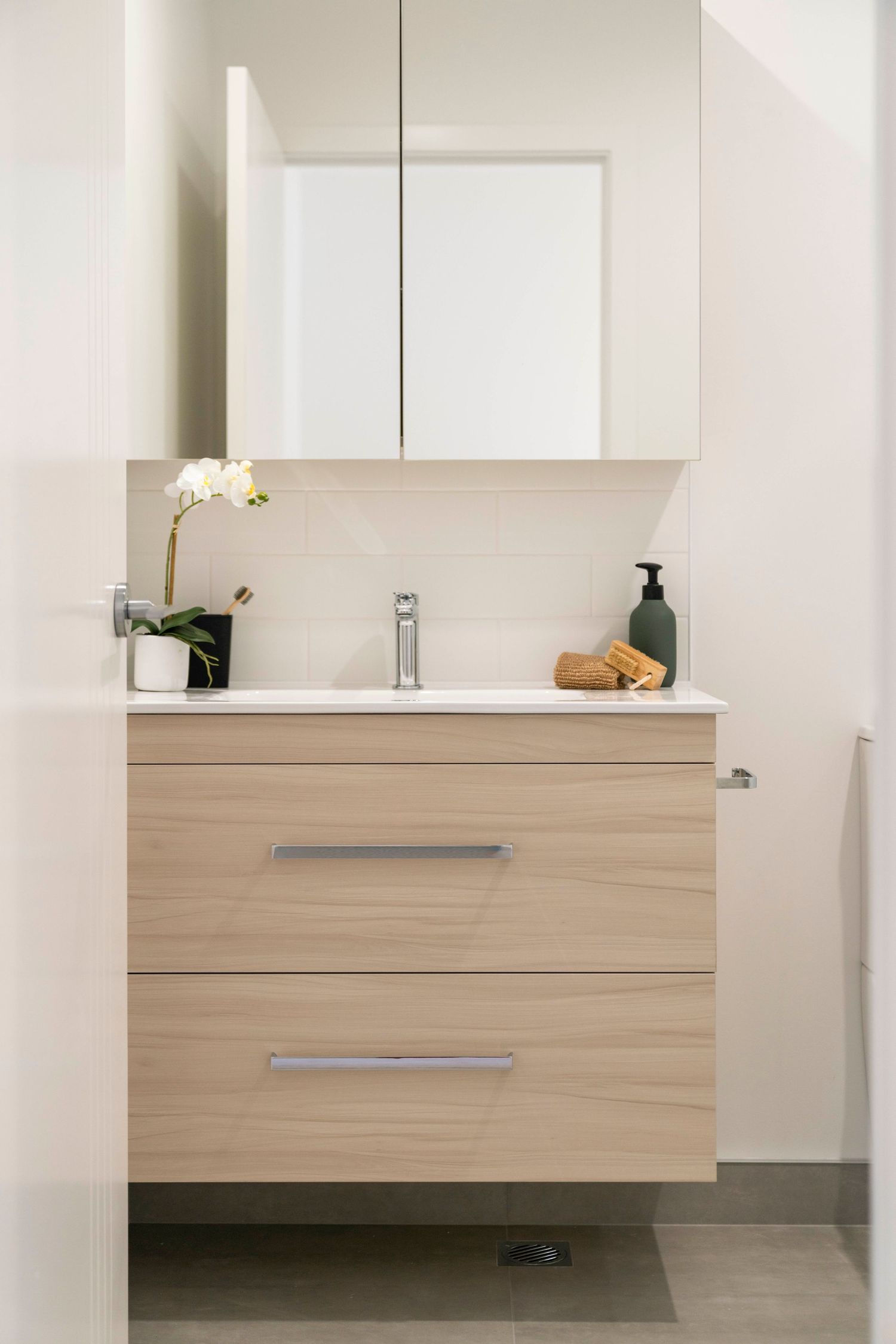 Modern floating vanity in light wood with white countertop and medicine cabinet.