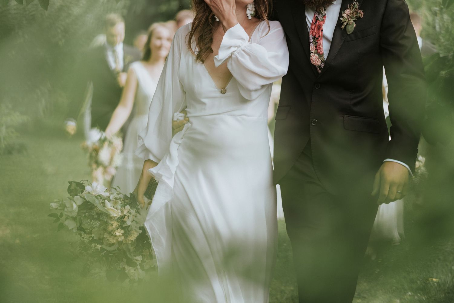 A newlywed couple walking together through lush green foliage in an intimate outdoor garden setting.