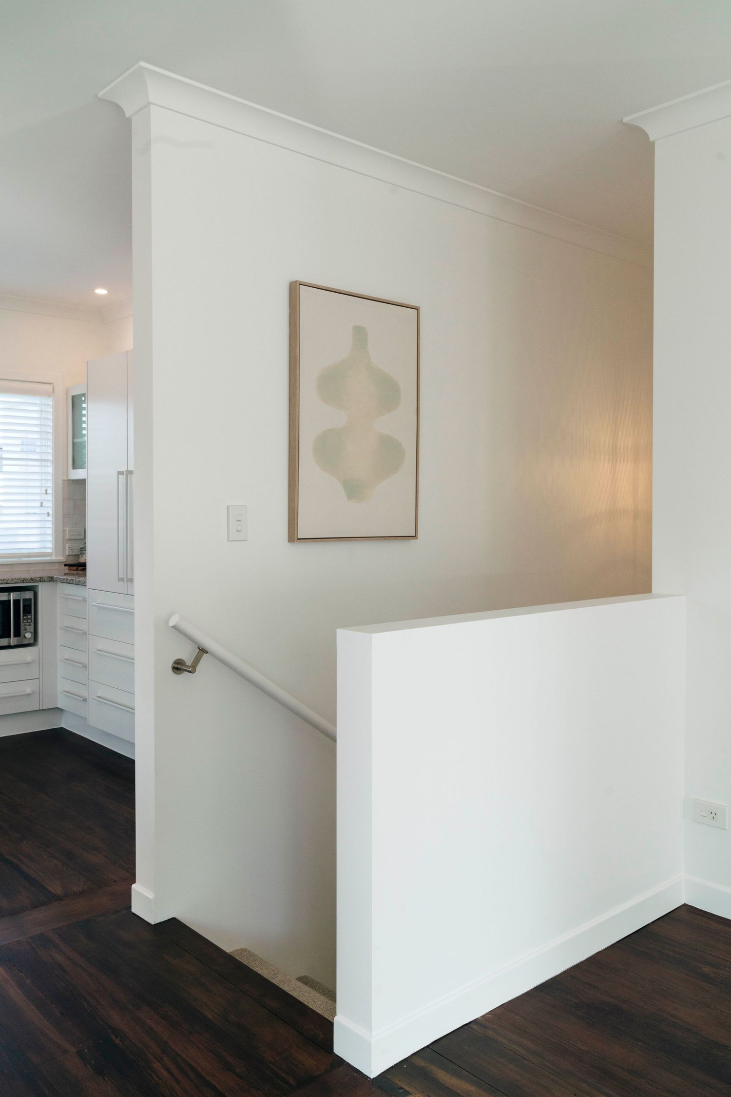 Modern hallway with crisp white walls, dark hardwood flooring, and subtle wall art.