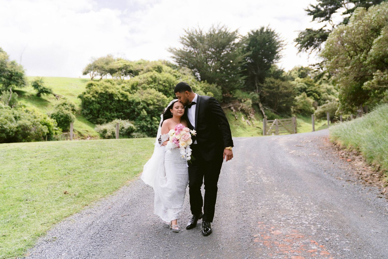 Wedding couple and guests walking along a scenic pathway surrounded by lush green hills.