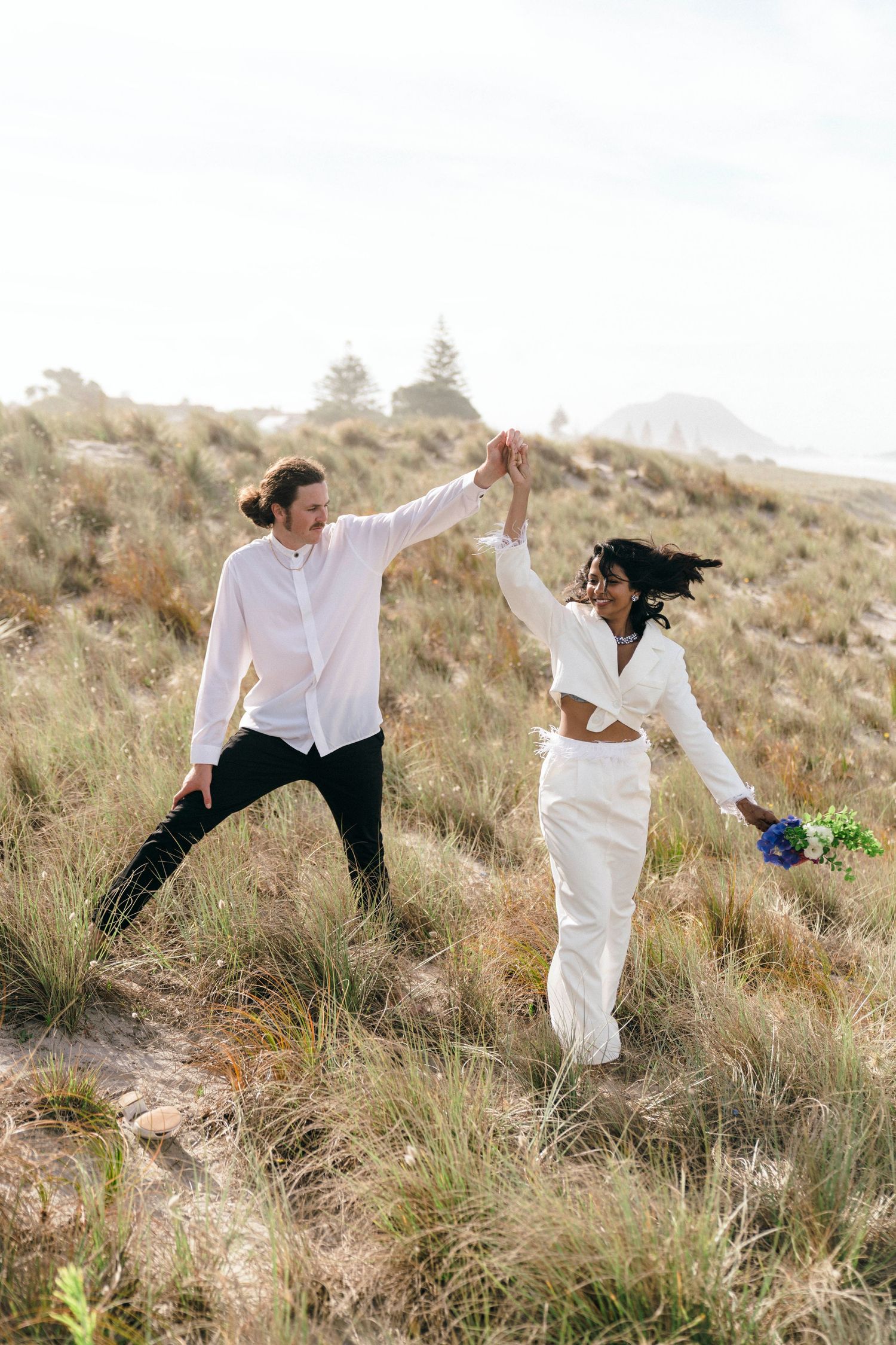 A celebratory dance pose between two people on a grassy hillside near the ocean.