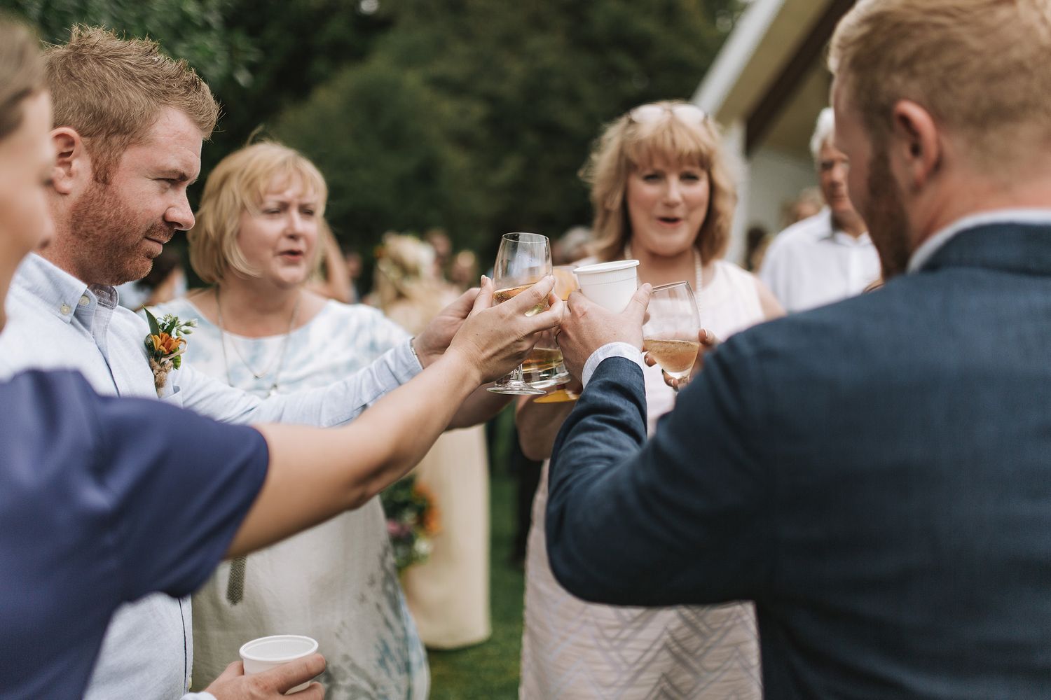 A group of wedding guests dancing and mingling in an outdoor garden reception with natural lighting.