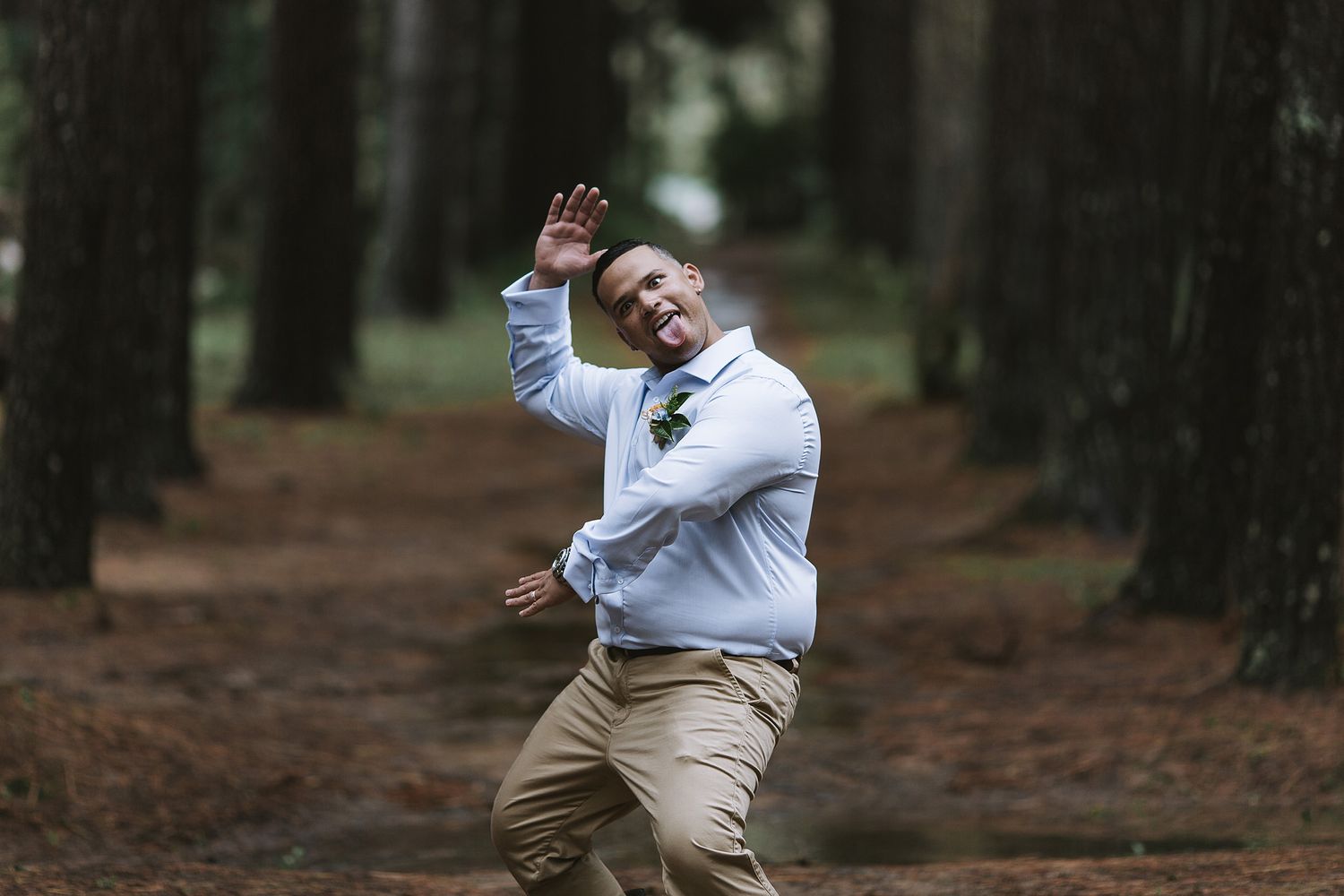 A person in a white sweater and khaki pants joyfully jumping and dancing through a forest path.