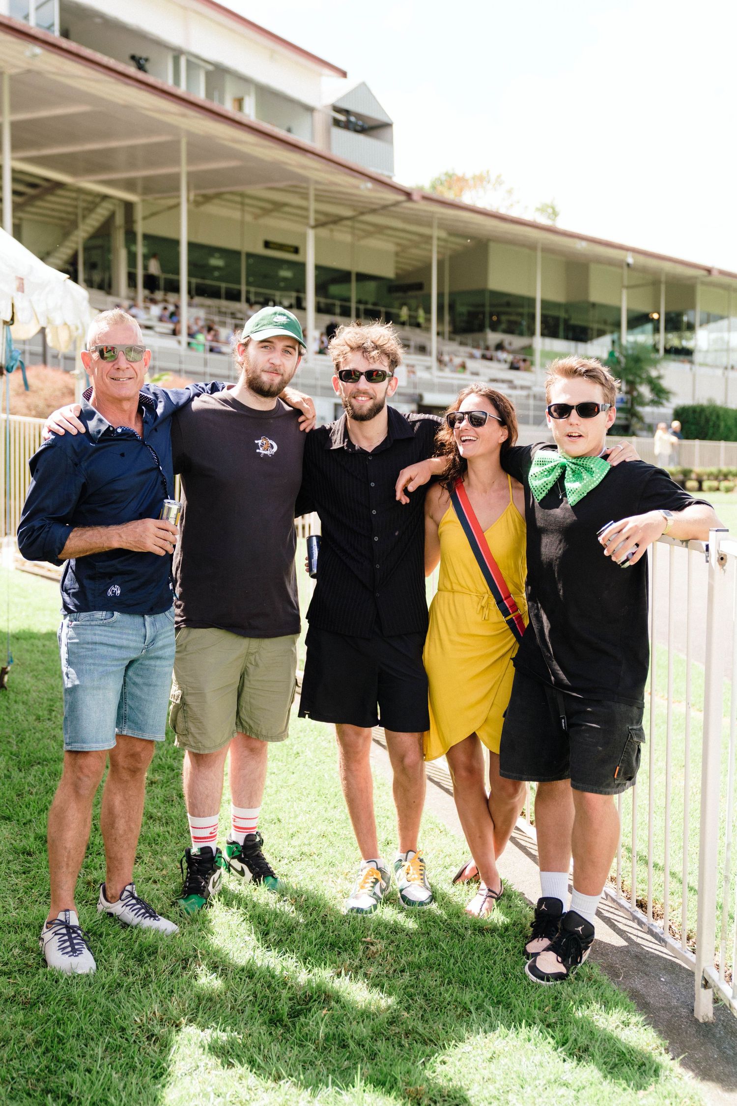 A row of friends in casual attire leaning against a white fence outdoors.