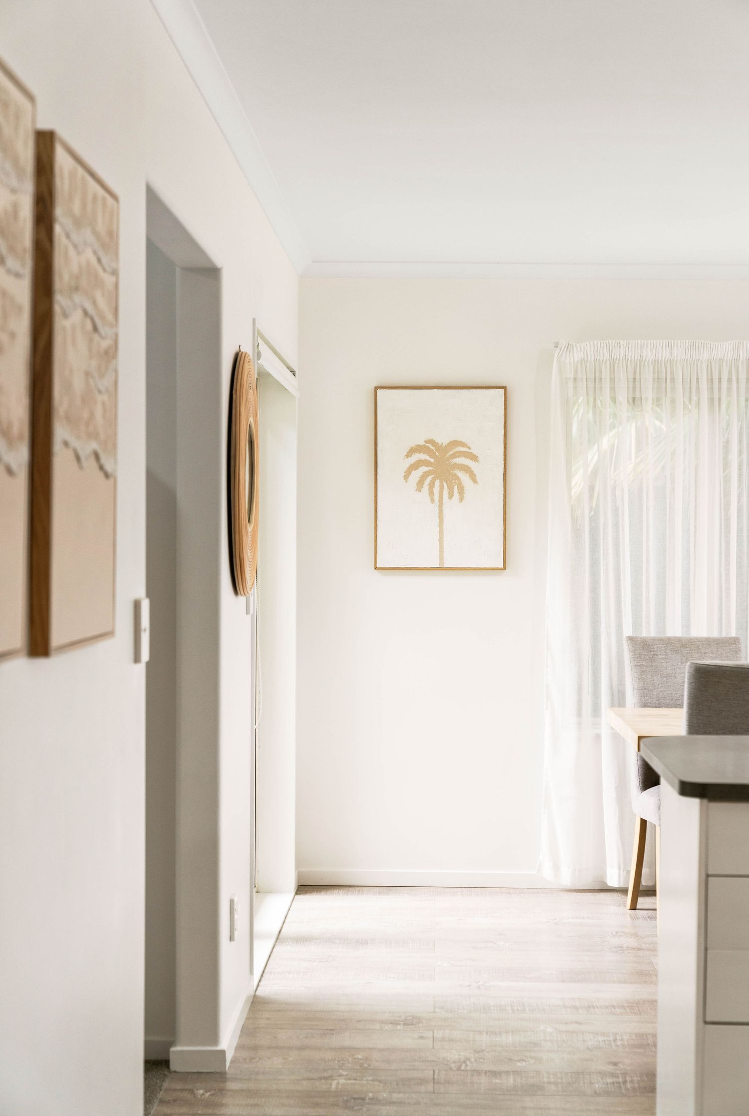 Modern hallway with white walls, hardwood flooring and a minimalist palm tree art print in a gold frame.