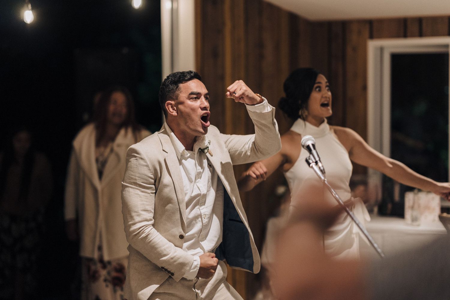 Wedding party celebrating with joyful dancing inside a rustic wood-paneled venue.