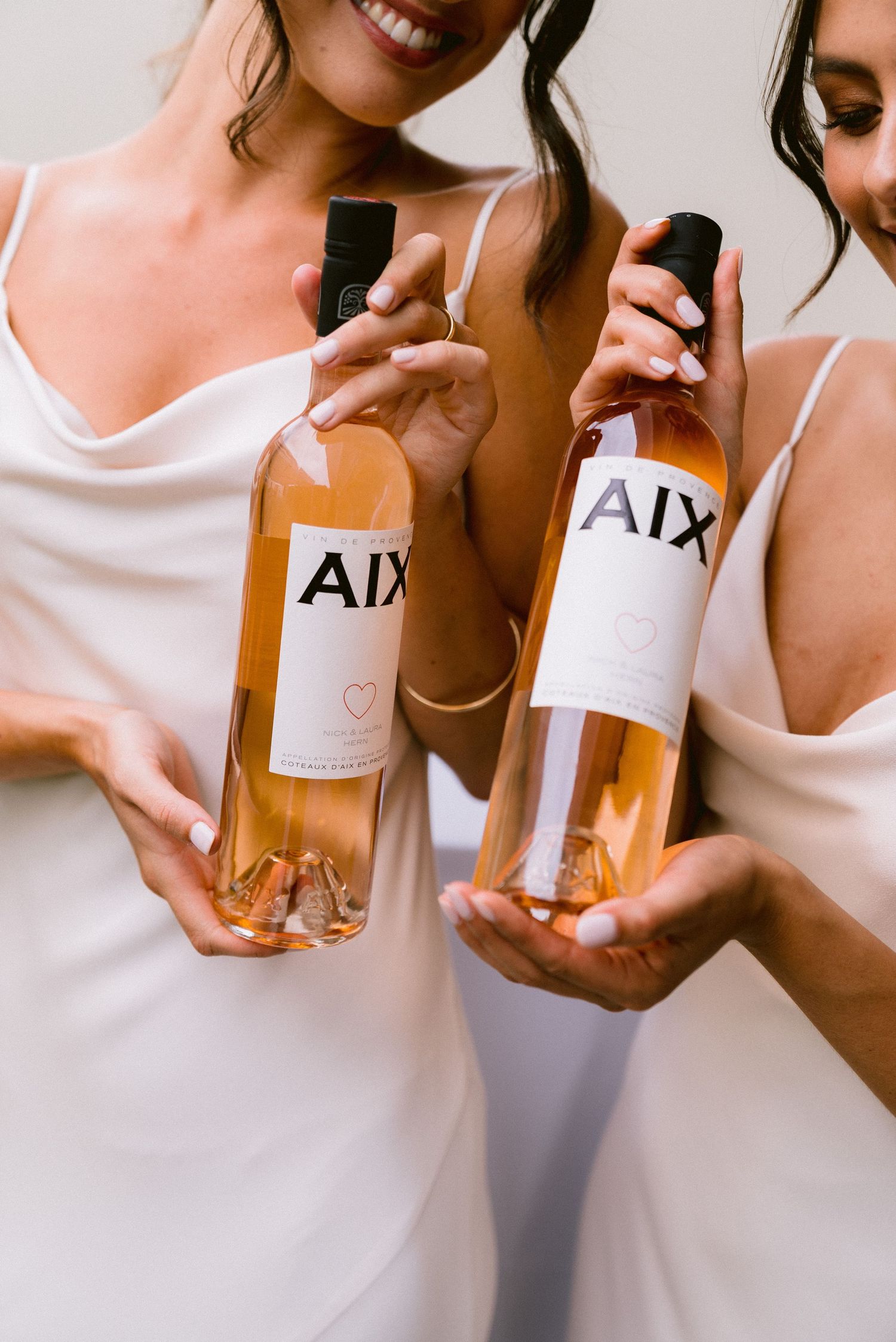 Group of friends holding matching rose wine bottles while wearing white tops during a celebration.