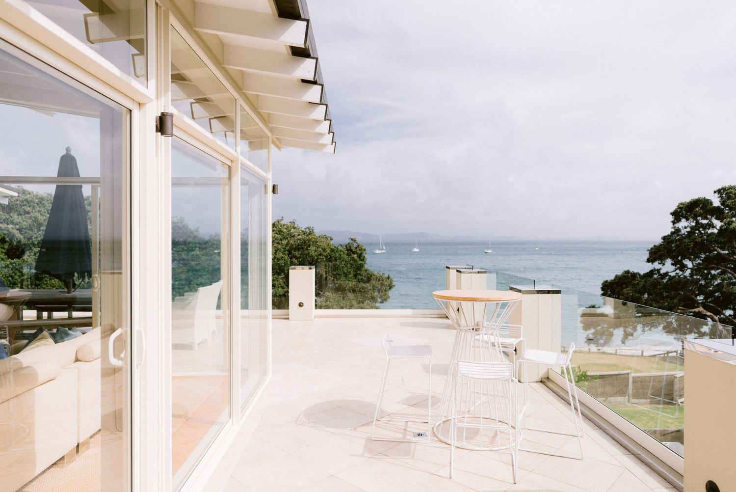 Modern white balcony overlooking a tranquil ocean bay with glass railings and minimalist patio furniture.