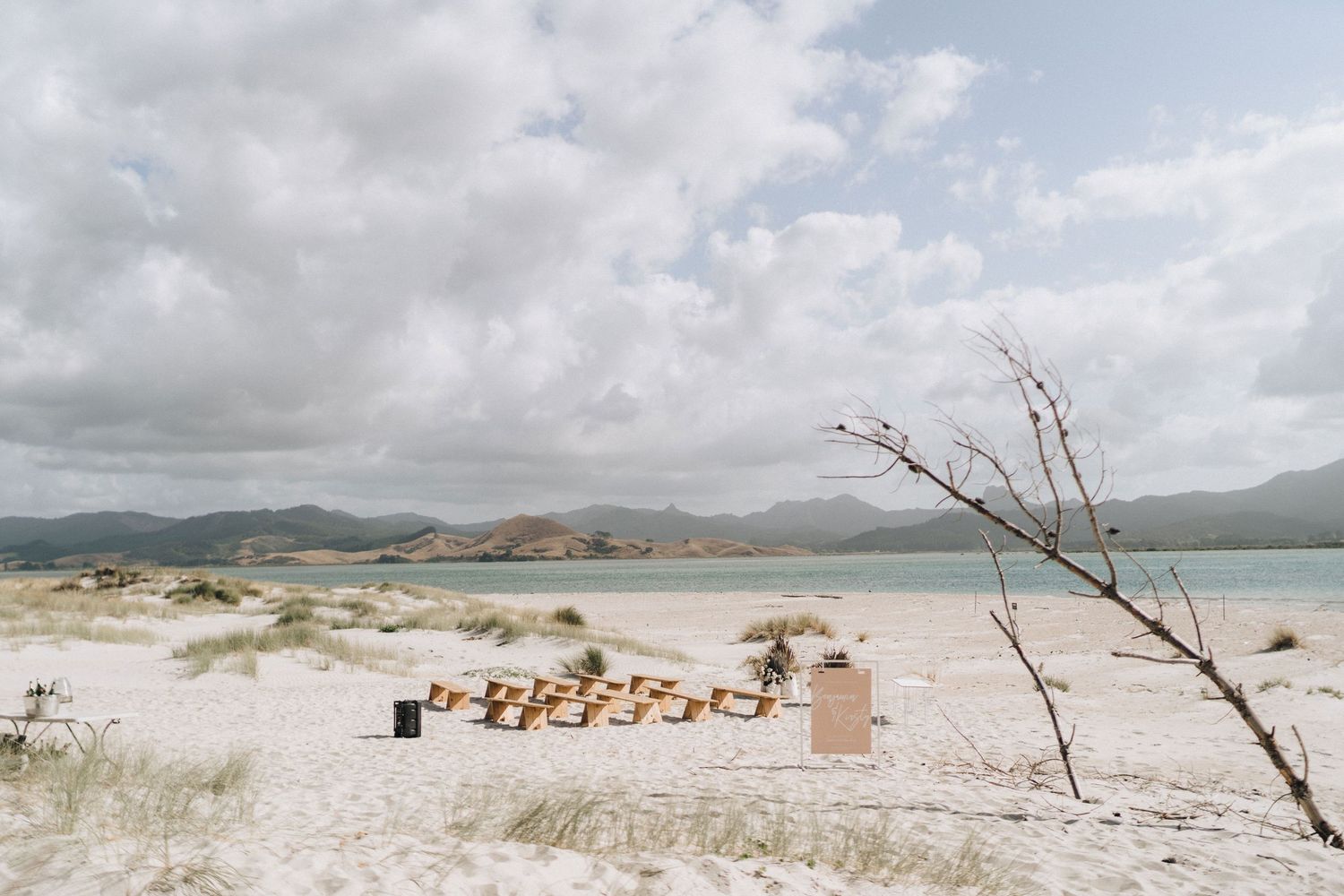 Panoramic view of a pristine white sandy beach with mountains and cloudy skies in the background.