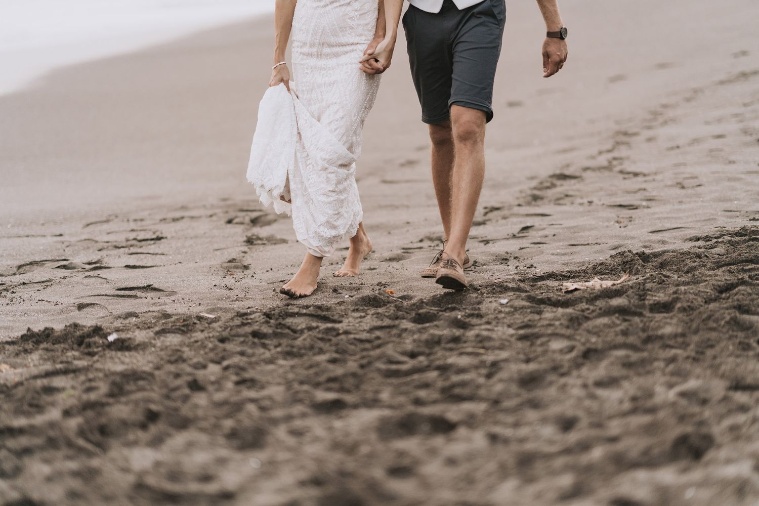 Couple walking hand in hand along a scenic beach shoreline at sunset.