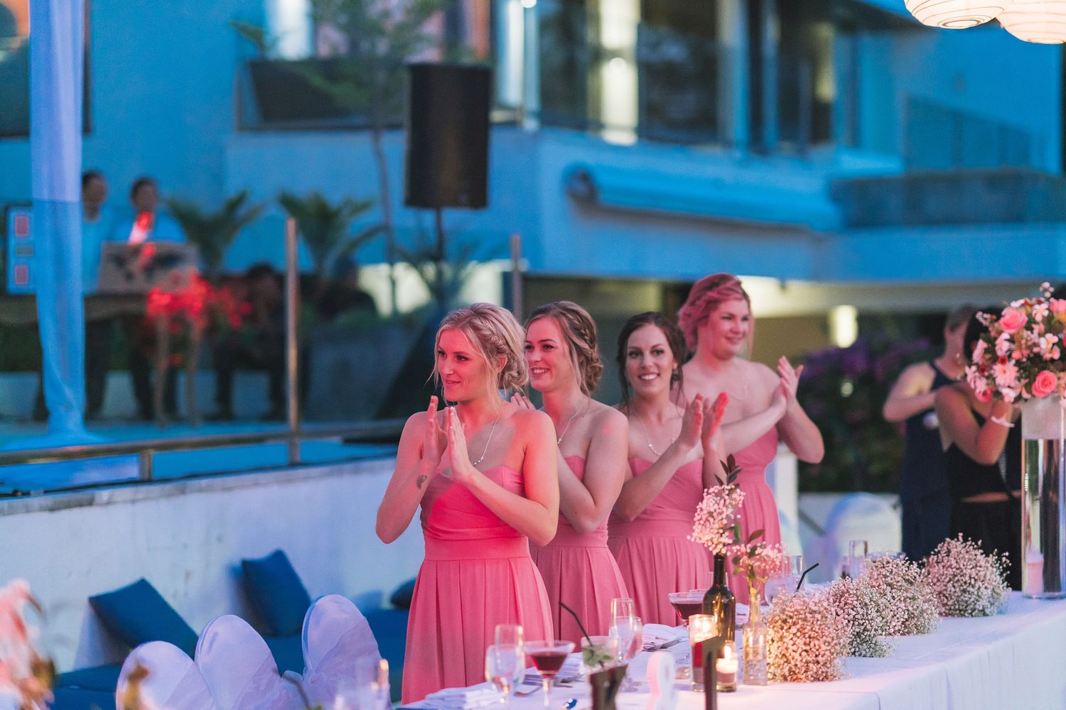 Wedding reception tables decorated in pink and blue lighting with guests seated for dinner.