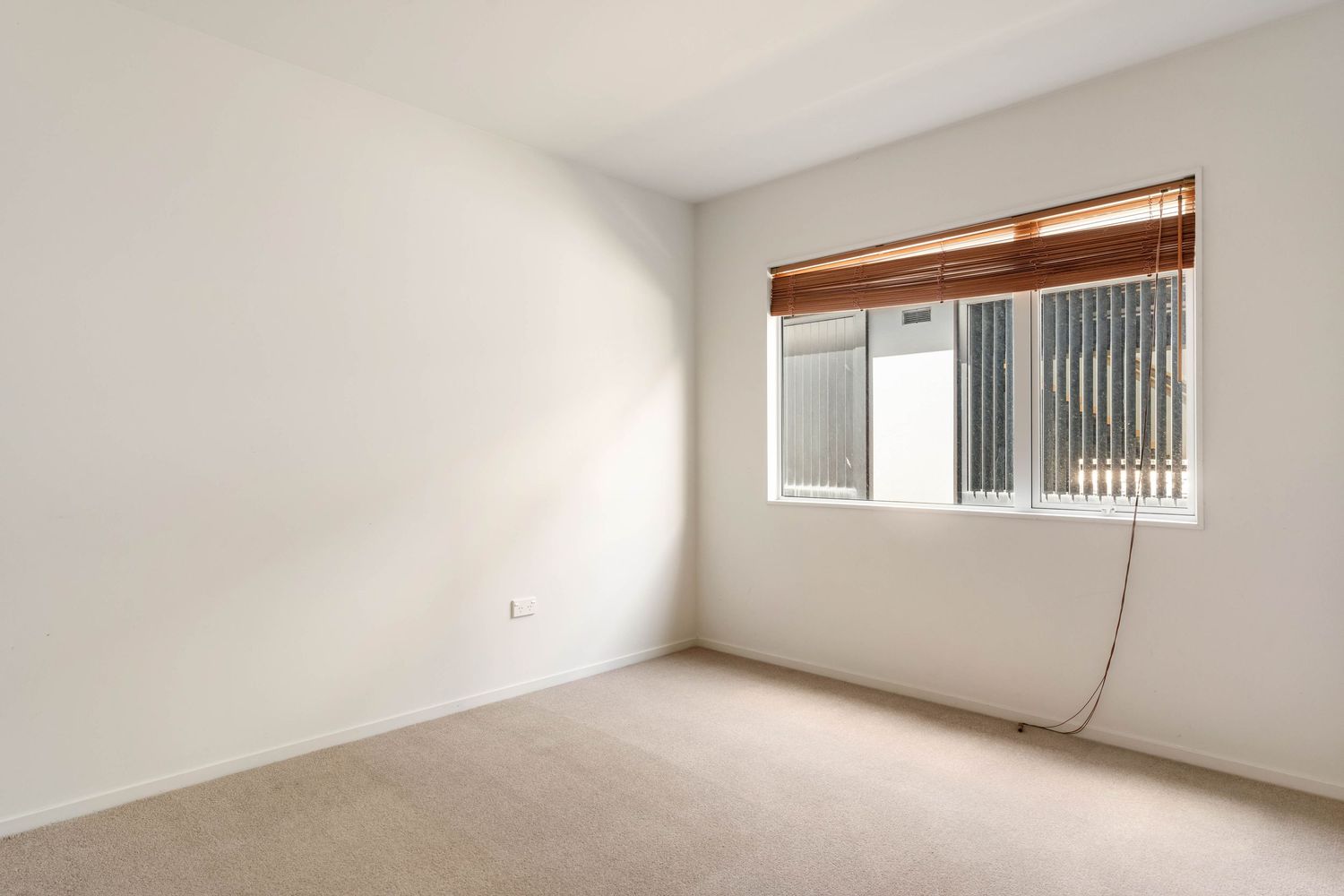 Empty bedroom with beige carpet, white walls and window with venetian blinds.
