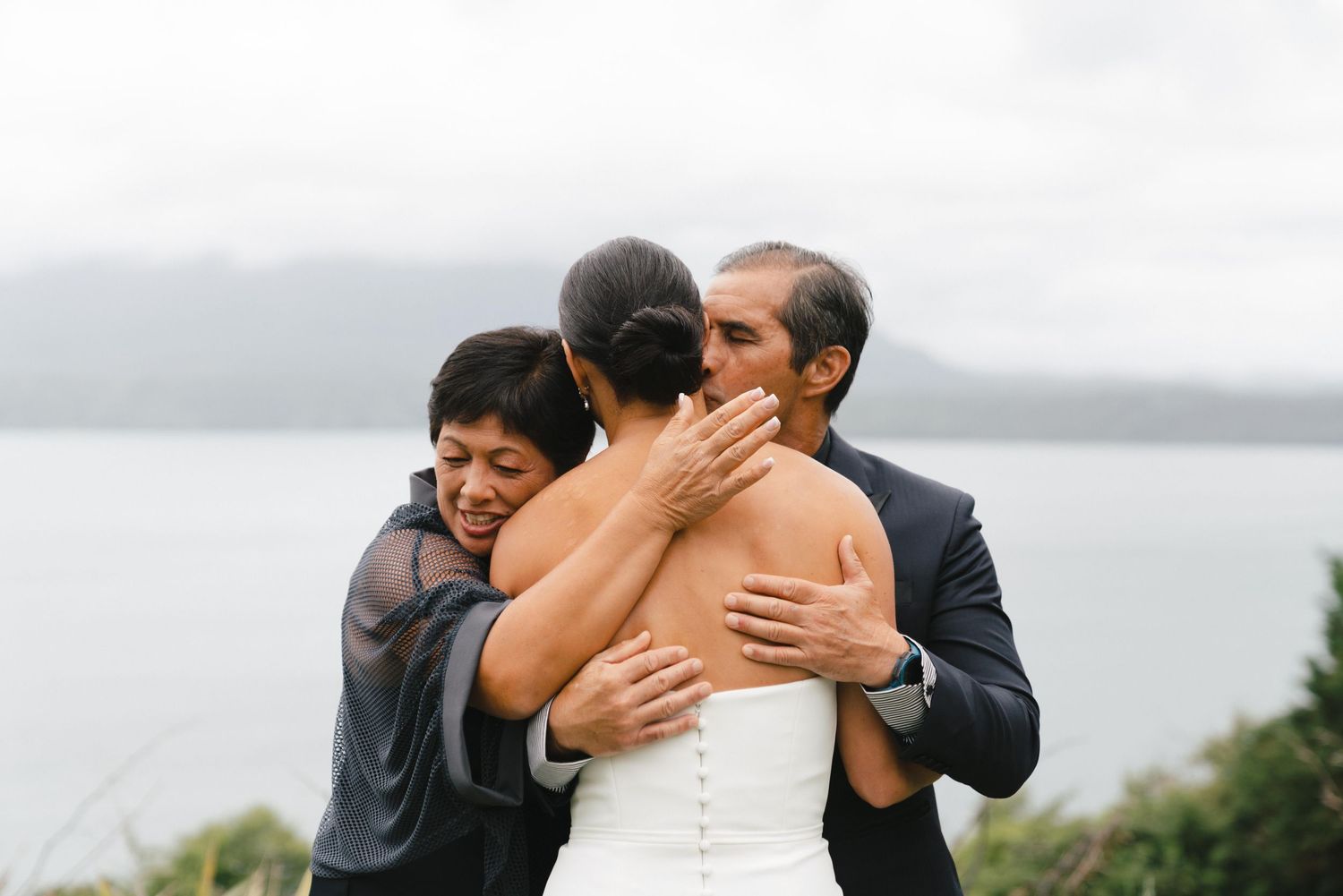 Religious couple embrace each other emotionally during their outdoor wedding ceremony by a serene lake.