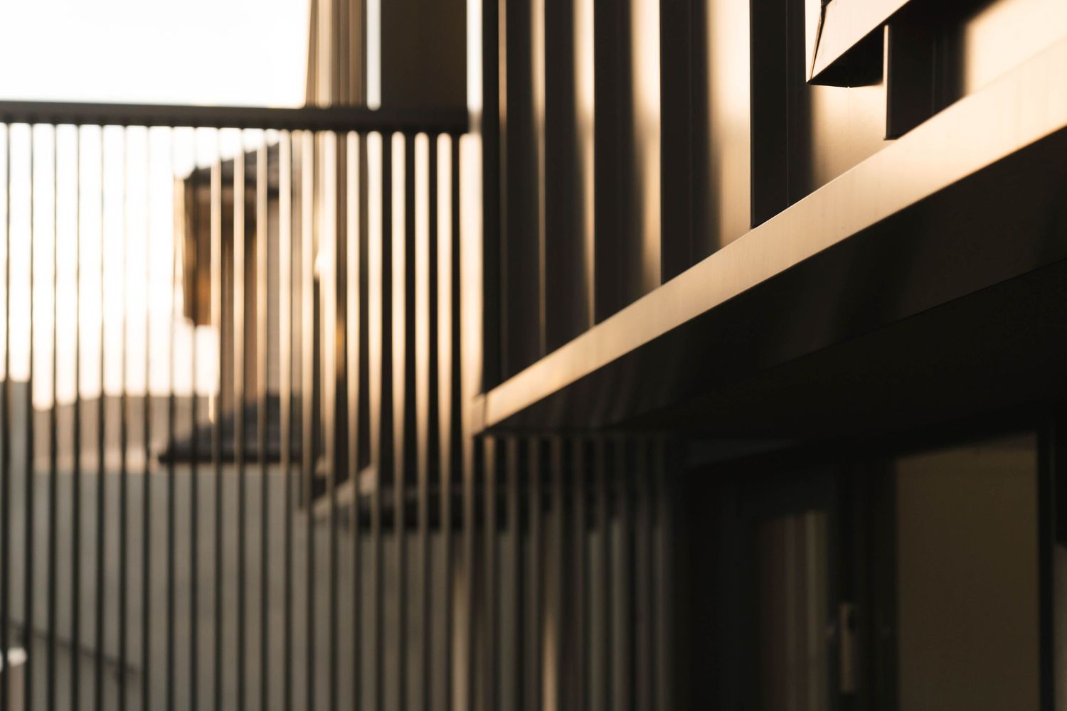 Architectural abstract of vertical metal slats with warm sunlight creating dramatic shadows and geometric patterns.