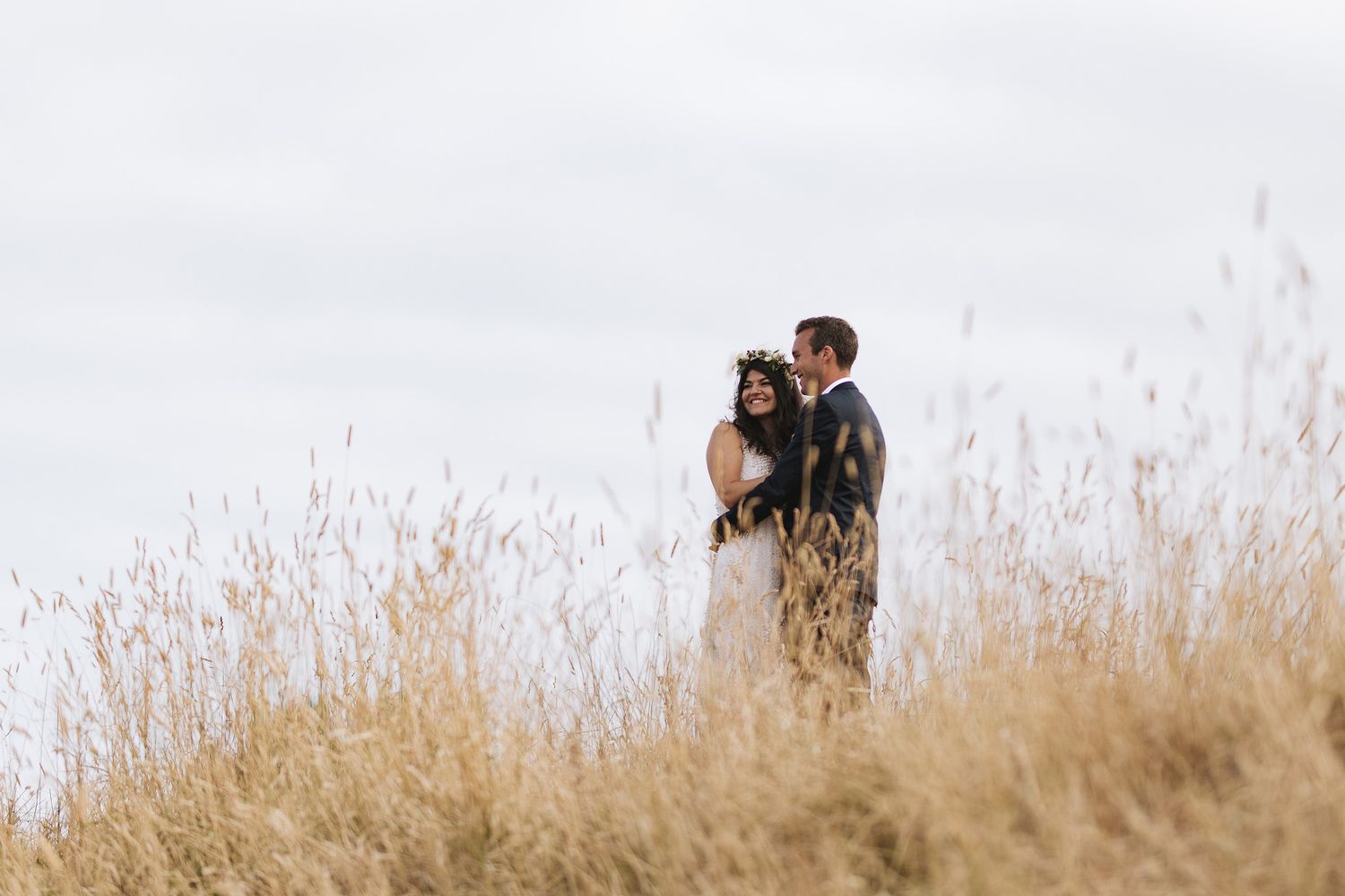A couple embraces in a sunlit field of tall golden grass during an intimate outdoor photo session.
