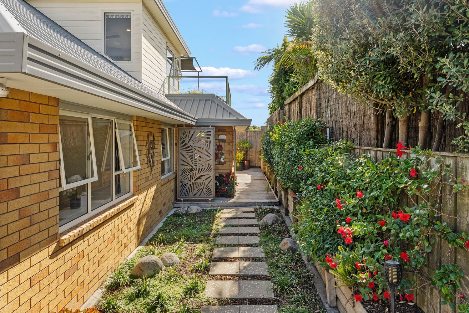 Brick house exterior with a garden pathway lined with blooming red flowers and green plants.