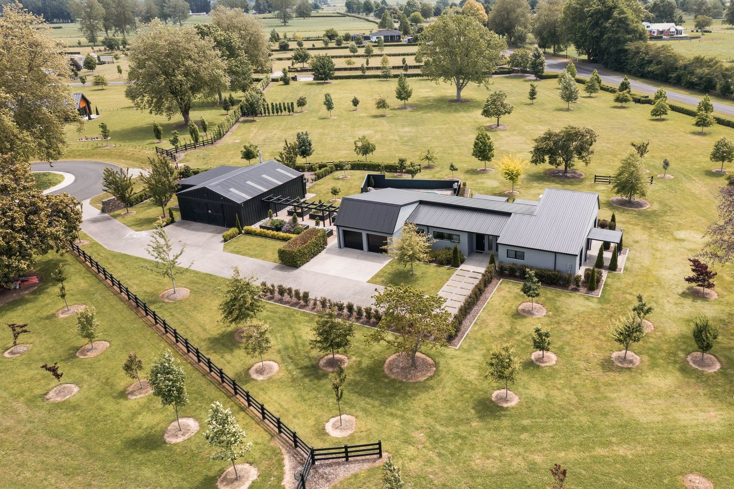 Aerial view of a rural property with multiple fenced paddocks and scattered trees on expansive green pastureland.