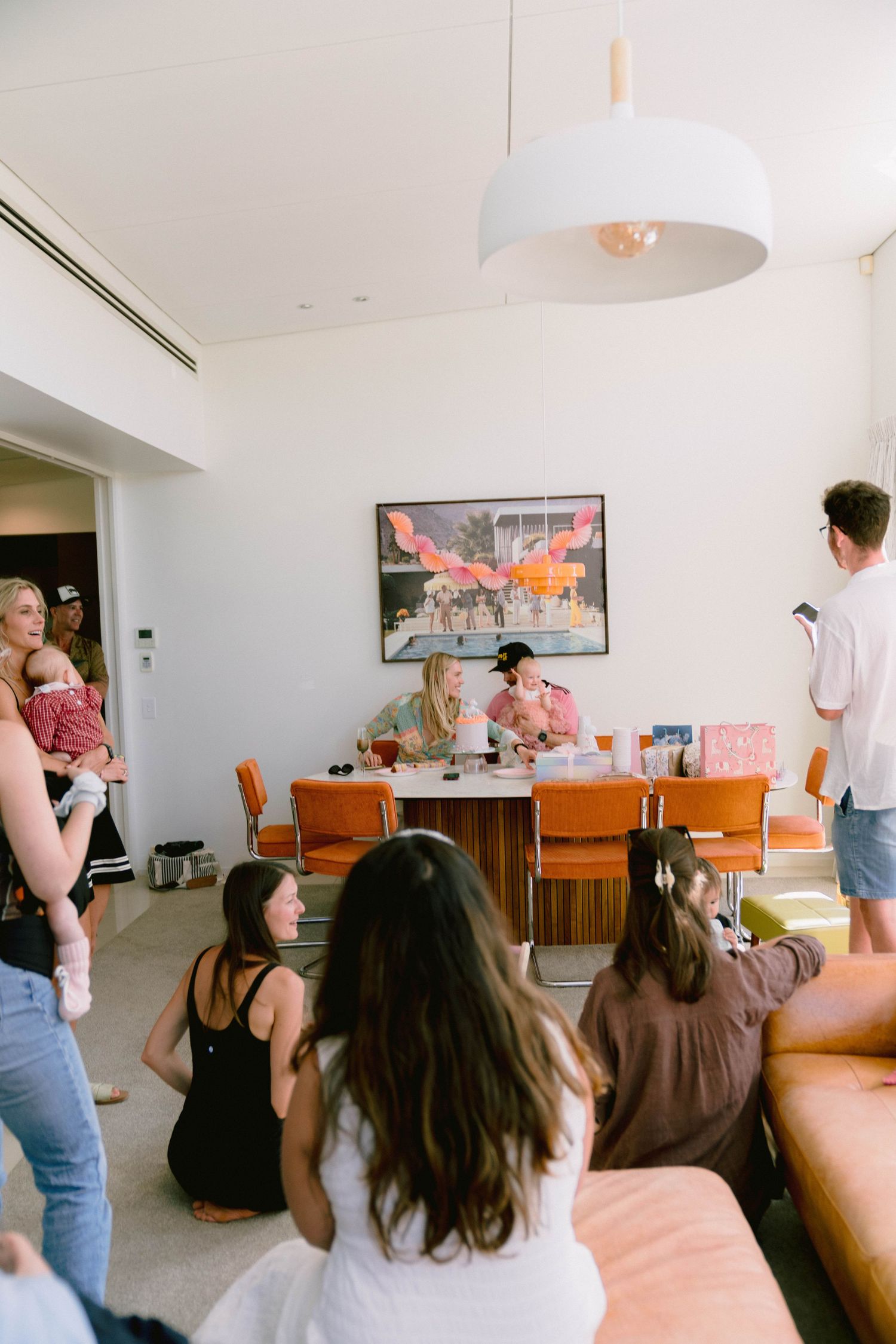 Modern living room gathering with people watching TV and lounging on orange furniture.