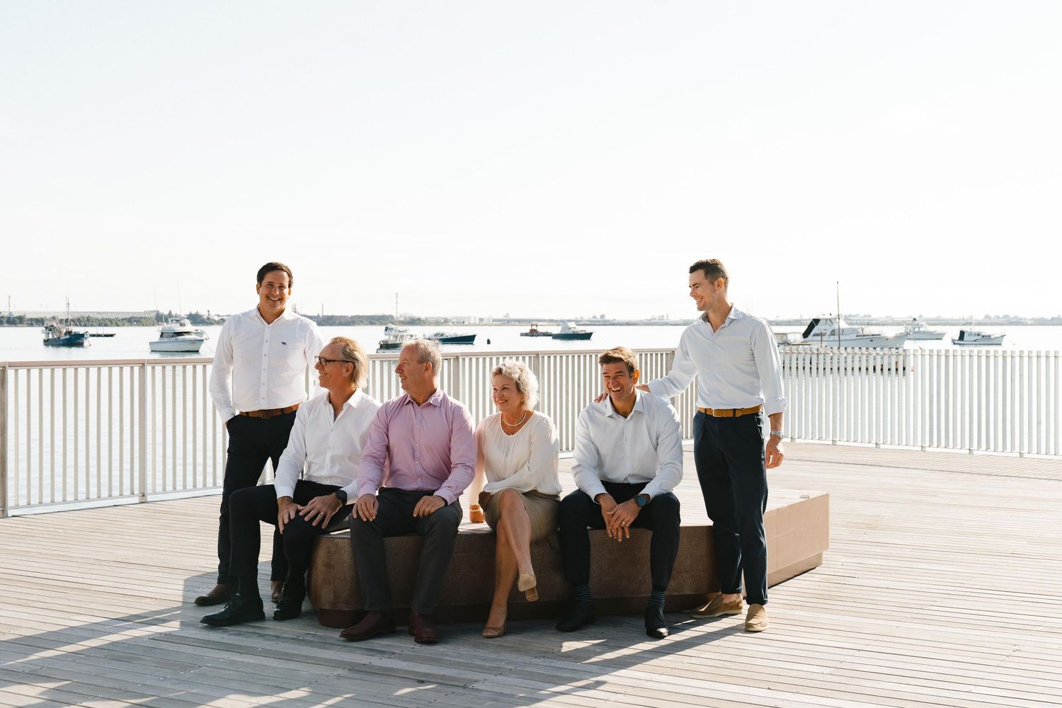 Professional group seated on a bench outdoors with a waterfront view behind them.