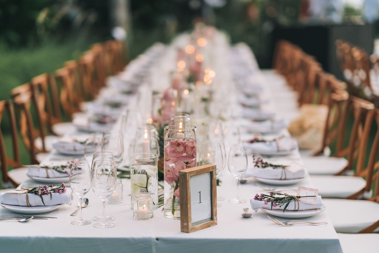 Elegant wedding table setting with white linens, place settings and pink floral centerpieces.