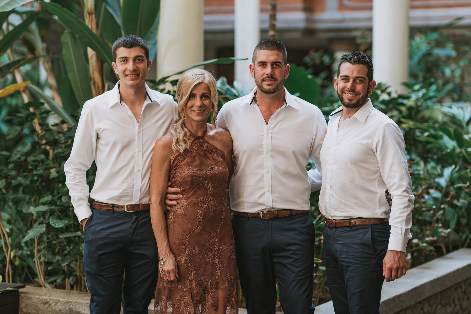 Family portrait of group in white shirts and brown dress standing by elegant columns and greenery.