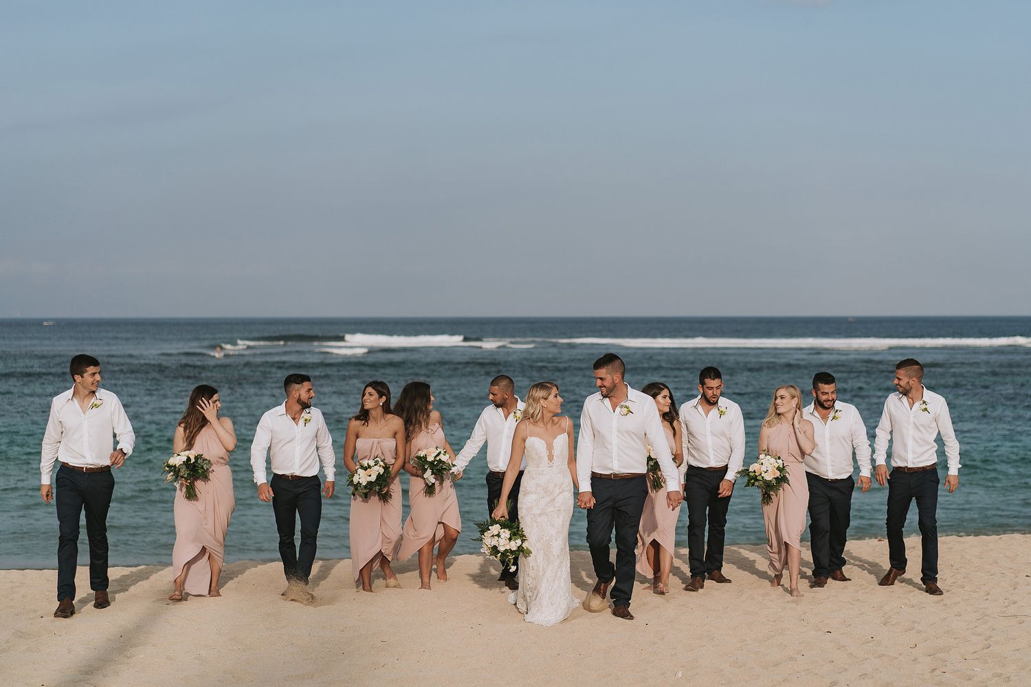 Wedding party poses together on a beach with ocean waves in the background.
