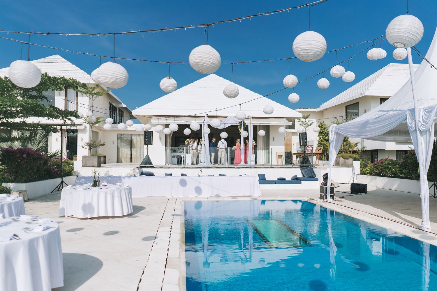 Poolside wedding venue decorated with white balloons and tables under a bright blue sky.
