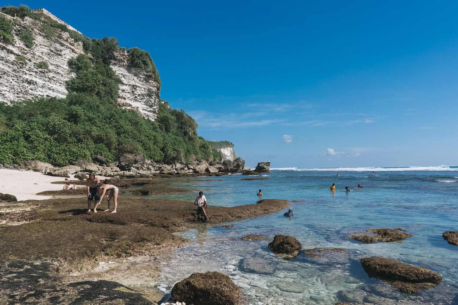 A scenic coastal view with white limestone cliffs meeting turquoise waters along a rocky shoreline under bright blue skies.