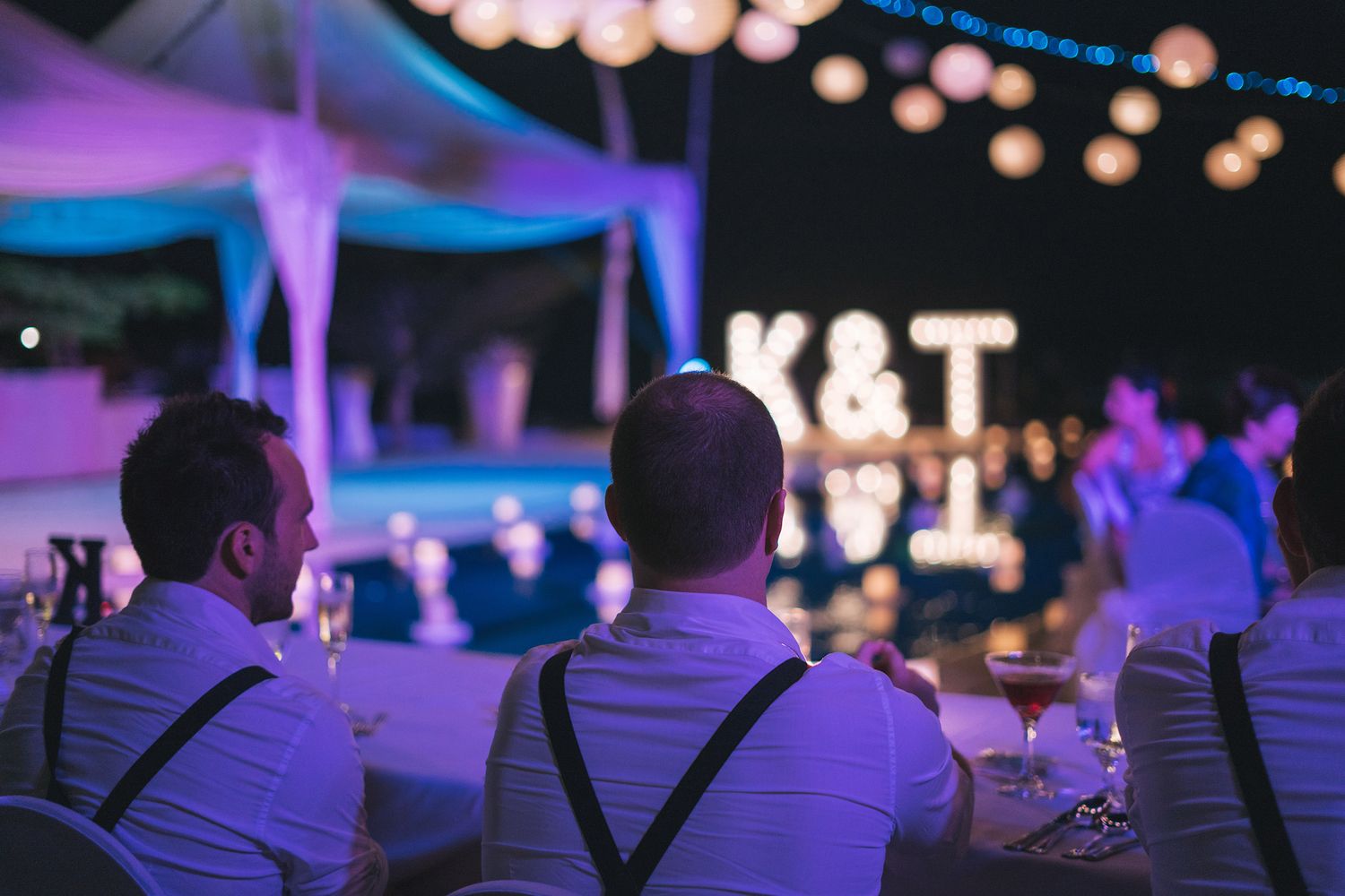 Purple and blue lighting illuminates guests with cameras at an evening outdoor event.