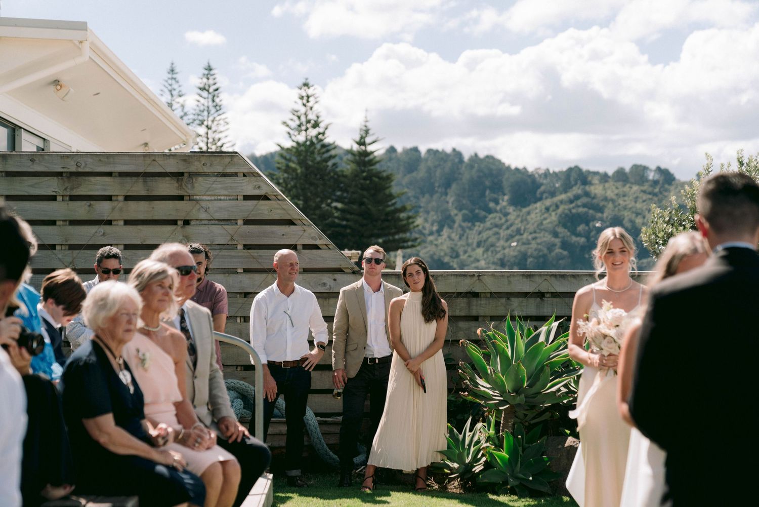 Wedding guests are seated outdoors at a scenic mountain venue during a ceremony.