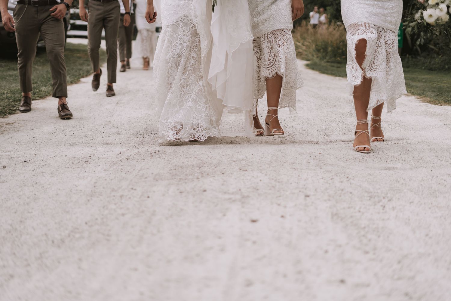 A group of people walking on a gravel path wearing white wedding dresses and formal attire with their feet in view.