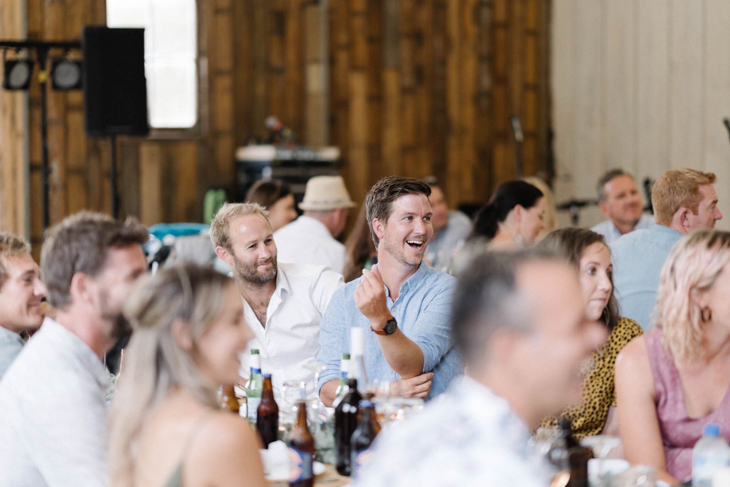 Wedding guests and family members mingle during a reception in a rustic barn venue with warm lighting and wooden decor.