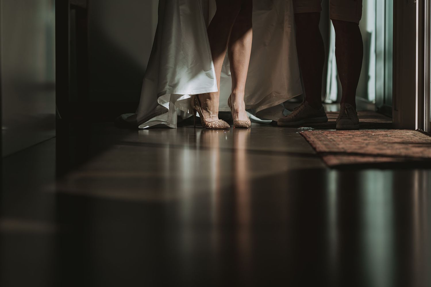 Bare feet visible beneath flowing curtains cast moody shadows on a dark hardwood floor in dim lighting.