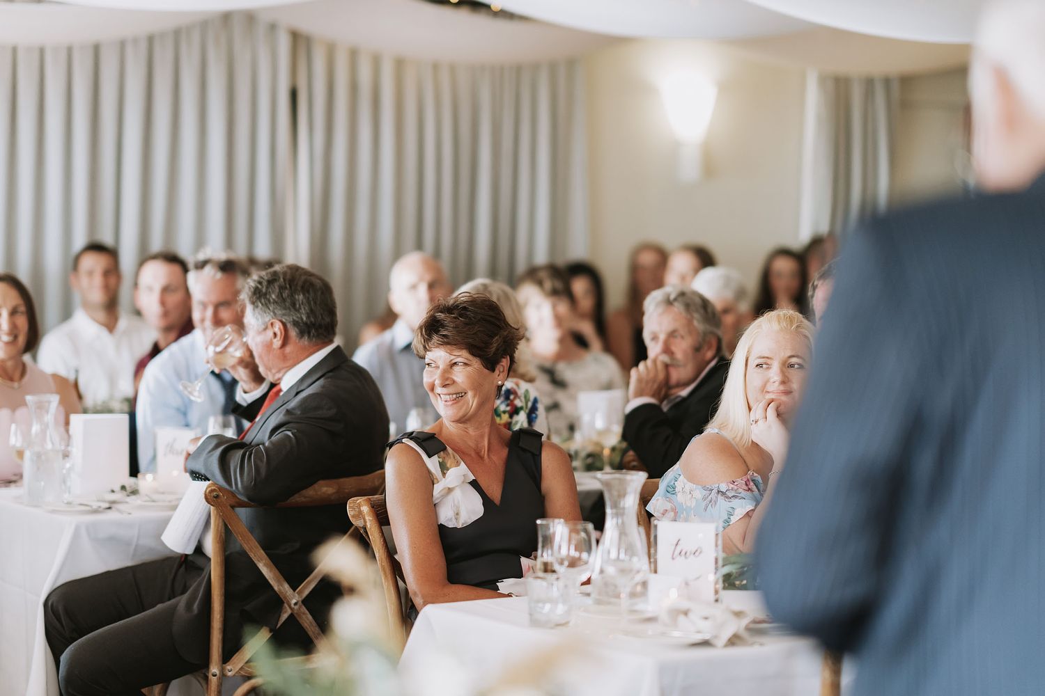 Wedding guests engaging in animated conversation during a reception dinner in an elegant banquet hall.