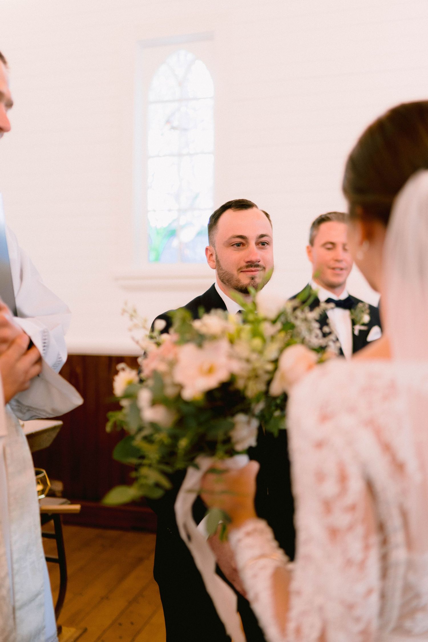 Wedding ceremony in a chapel with floral arrangements and stained glass windows.