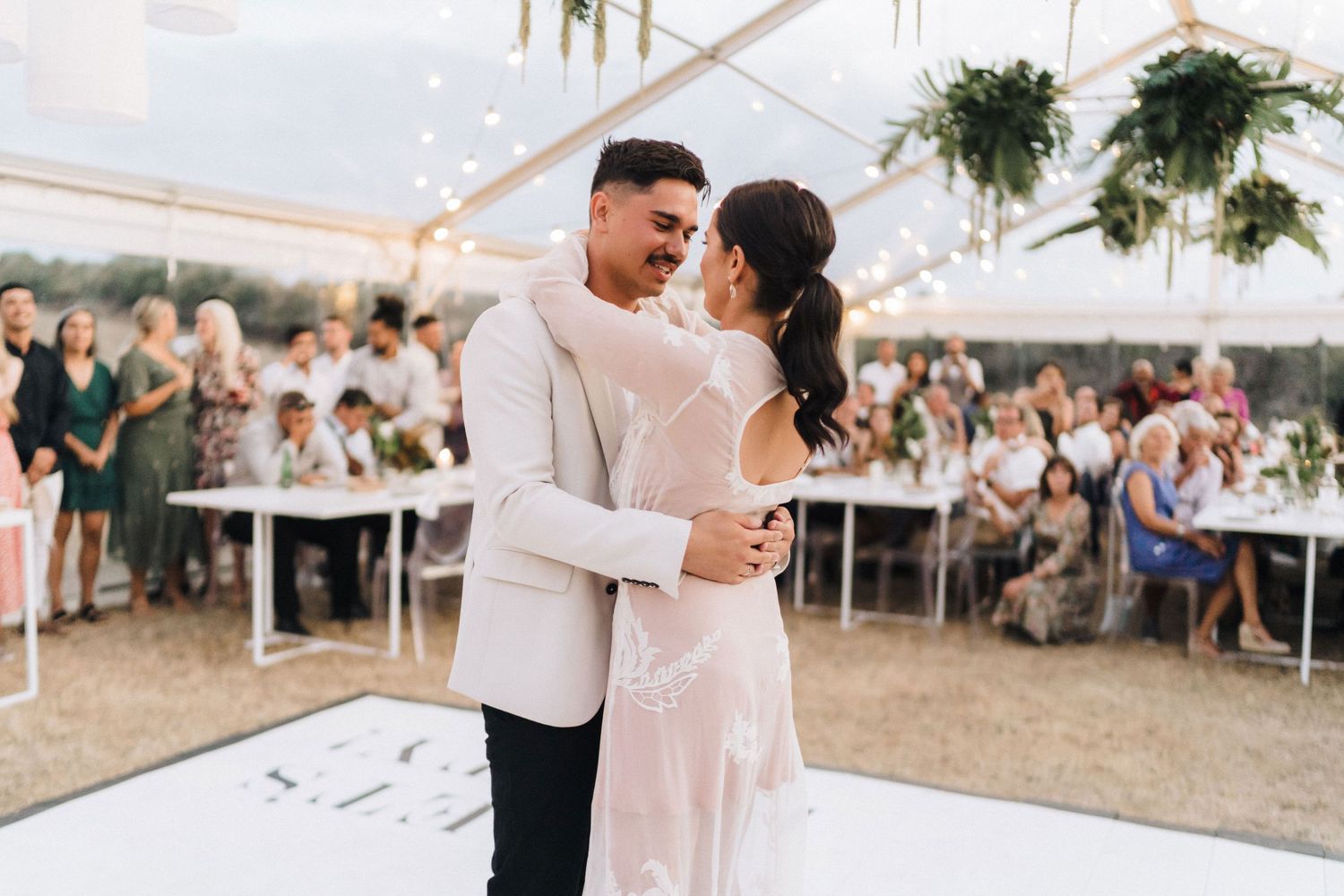 Couple shares their first dance under white tent at outdoor wedding reception.