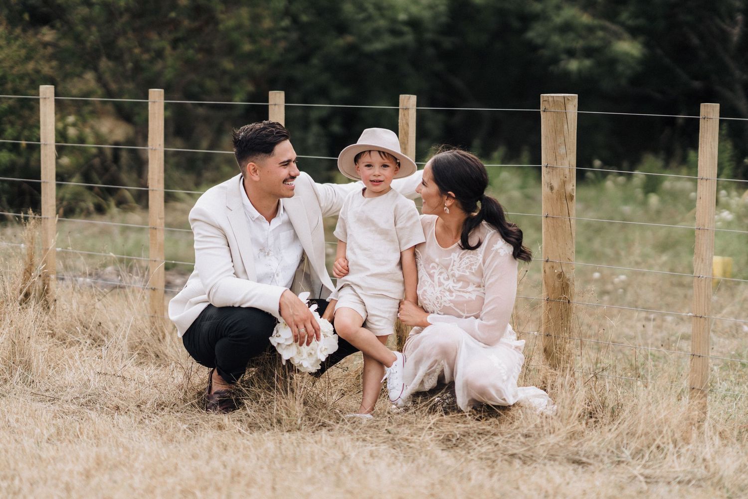 Family shares intimate moment sitting together on rustic fence in countryside setting.