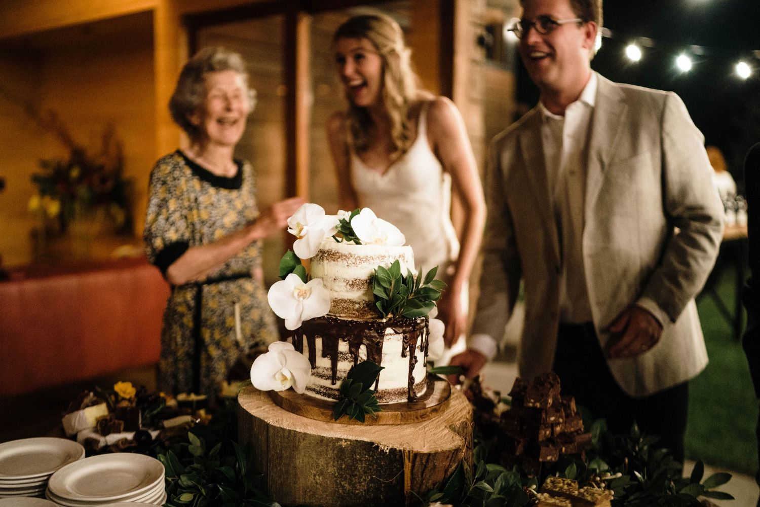 Wedding reception guests socializing at rustic wooden tables with ambient lighting.