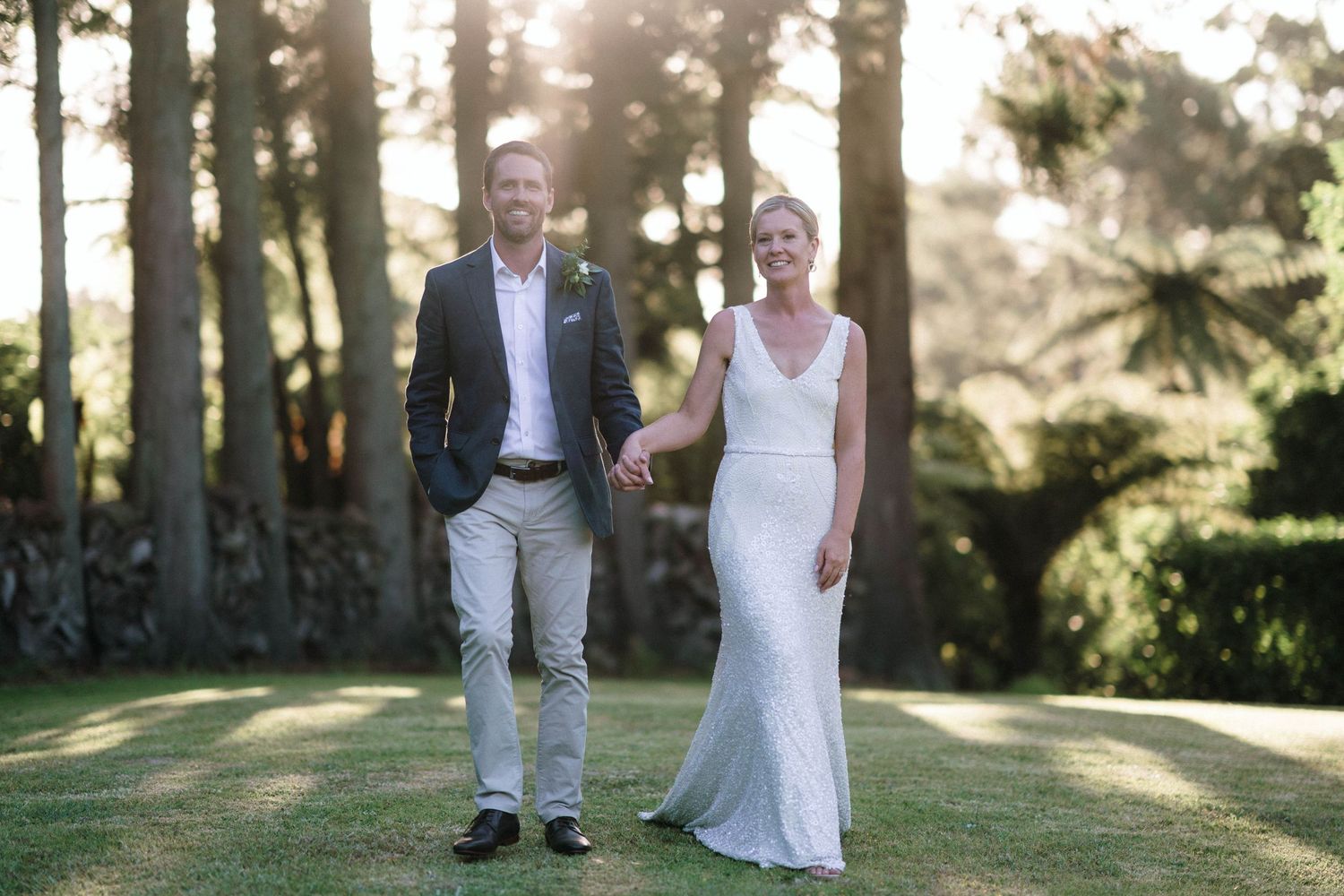 Romantic sunlit wedding portraits among tall trees at golden hour in a park setting.