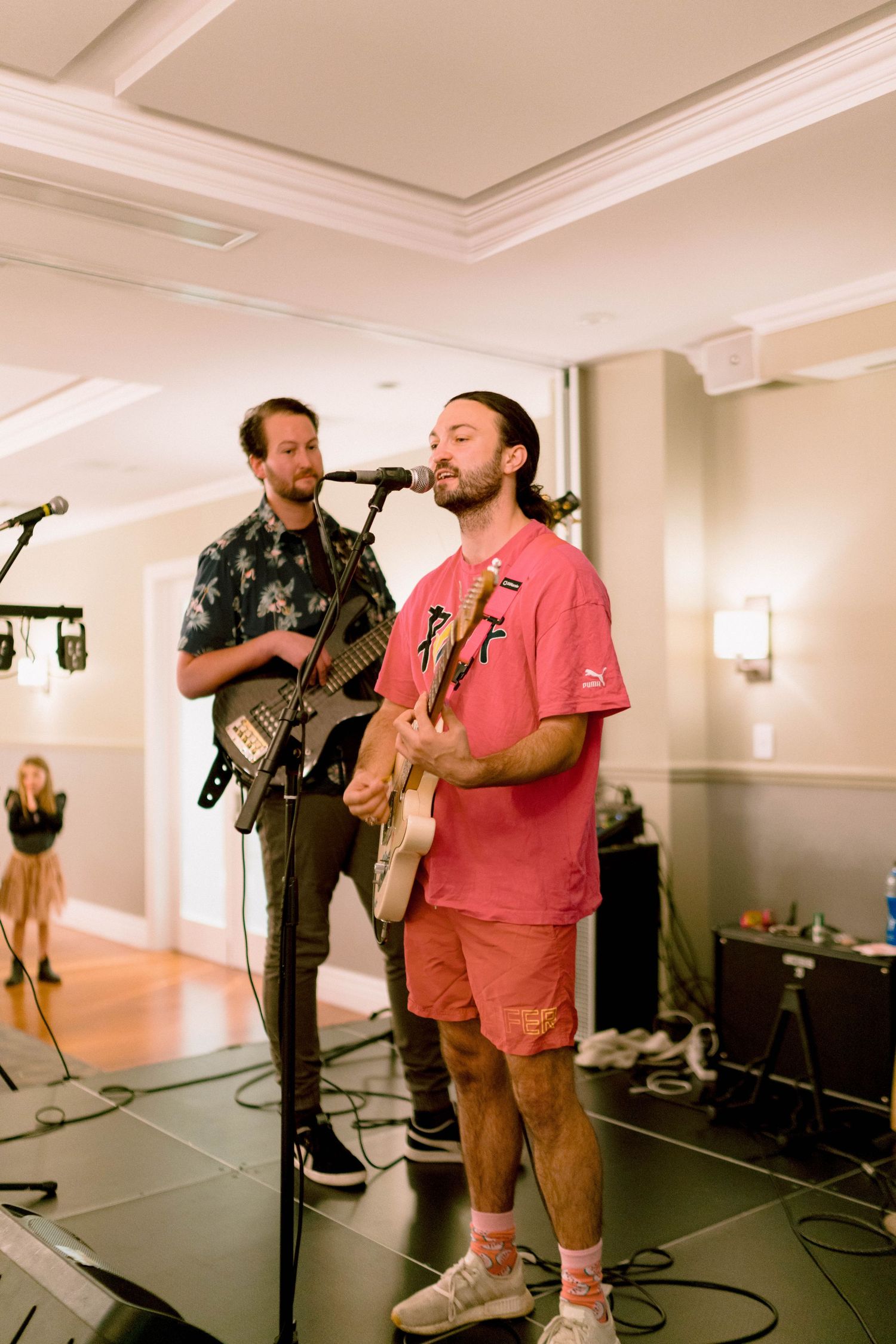 Two musicians perform on stage with guitars and microphones at an indoor event venue.