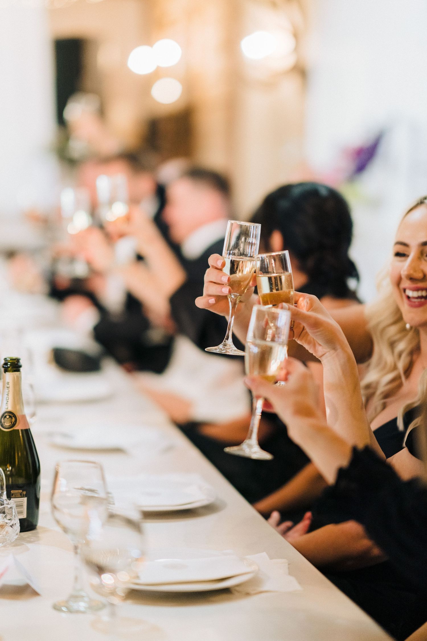 Wedding guests raise champagne glasses in a celebratory toast at an elegant reception dinner table.