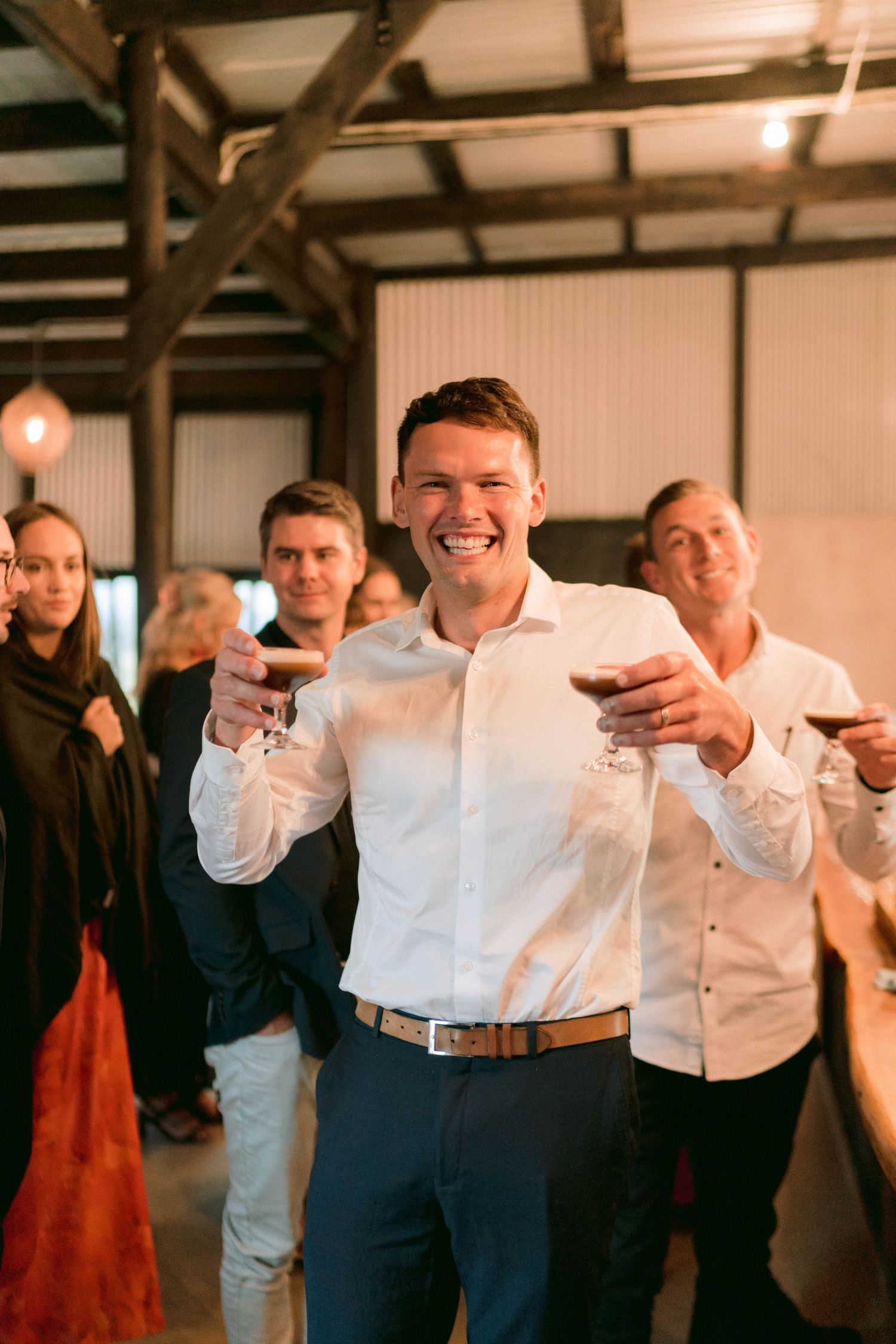 Wedding guests celebrating and laughing during an indoor reception in a rustic barn venue.