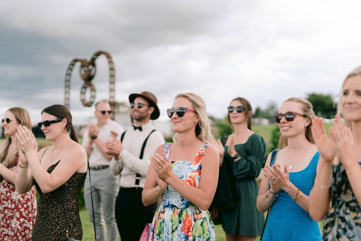 Wedding guests in colorful dresses applauding during an outdoor celebration.