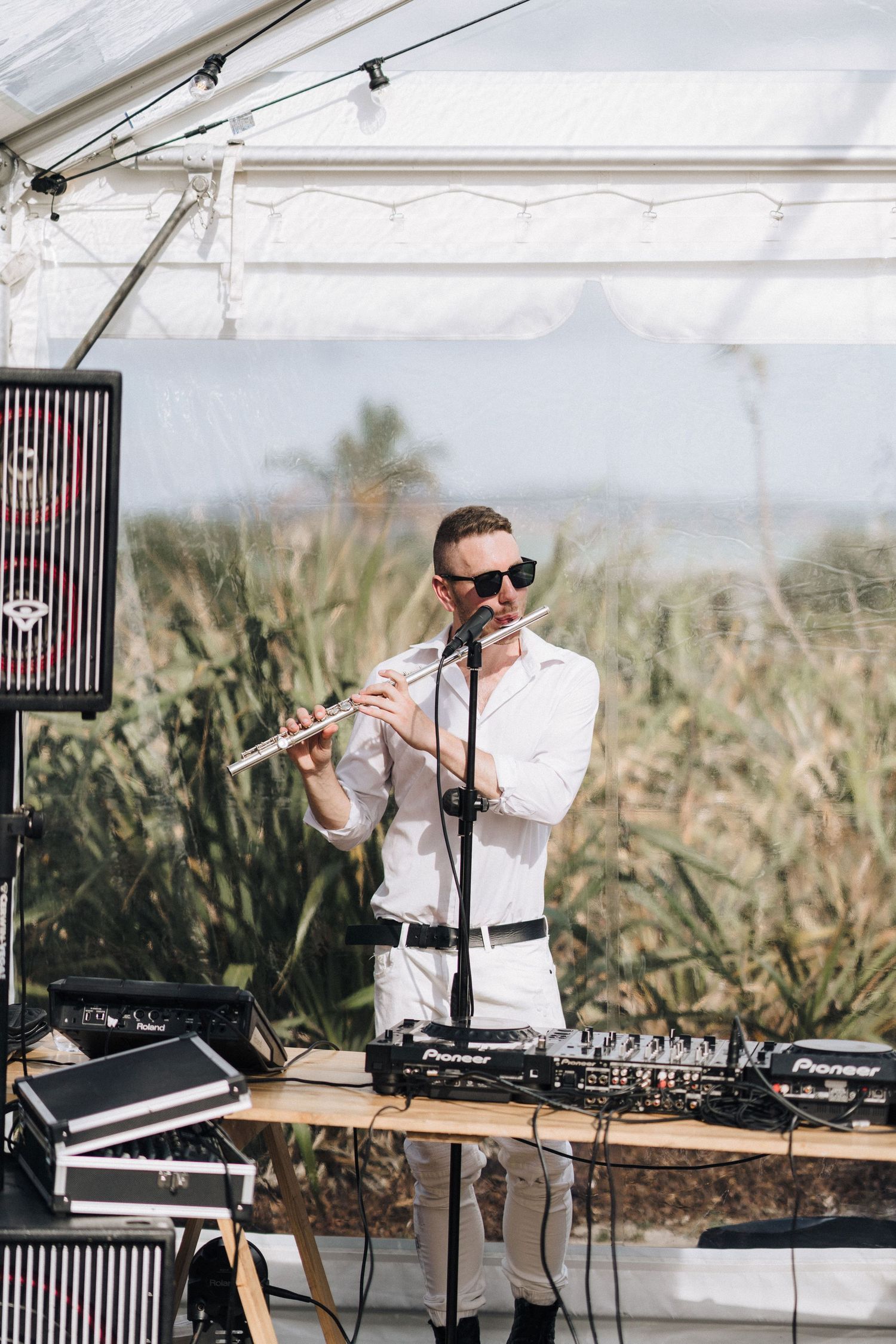 Professional musician in white performing with modern electronic music equipment under a white tent outdoors.